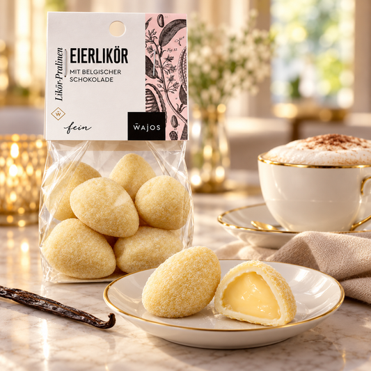 Eierlikör-Pralinen mit Anschnitt und Cappuccino auf weißem Porzellan im warmen Café-Ambiente